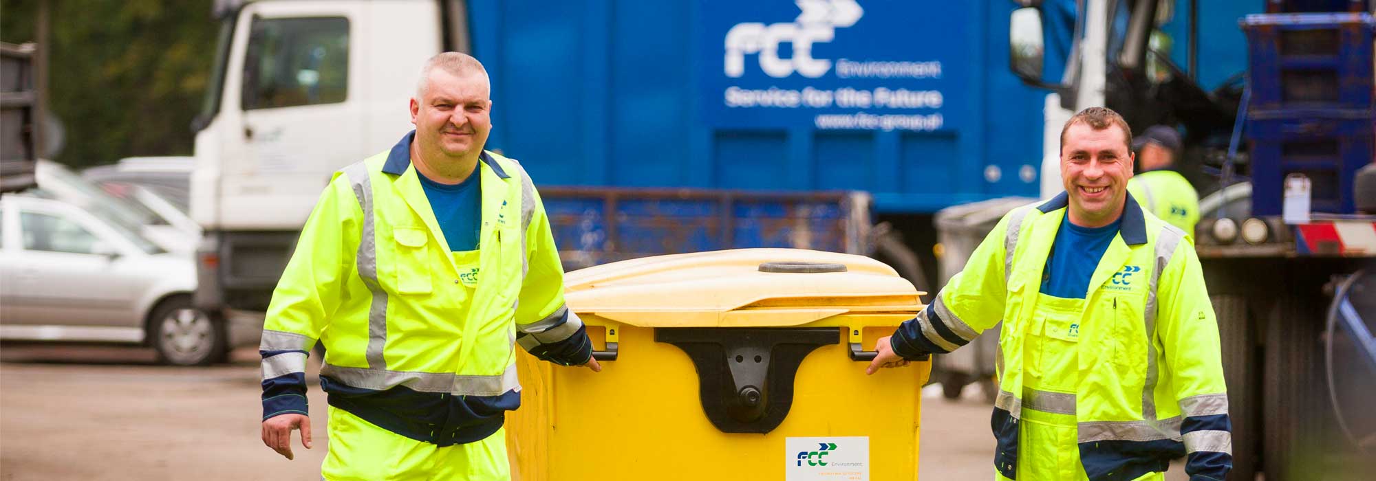 2 Männer mit einem gelben Müllcontainer im Hintergrund Abfallfahrzeug von FCC Abfall Service online